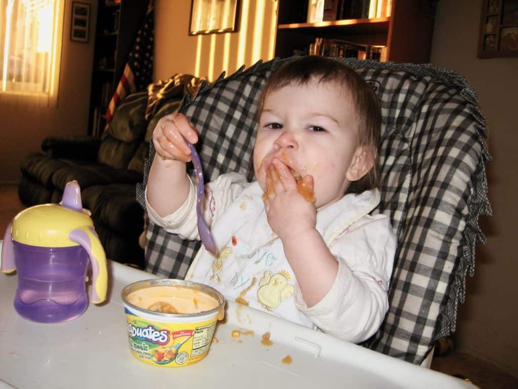 Toddler eating food in a high chair.