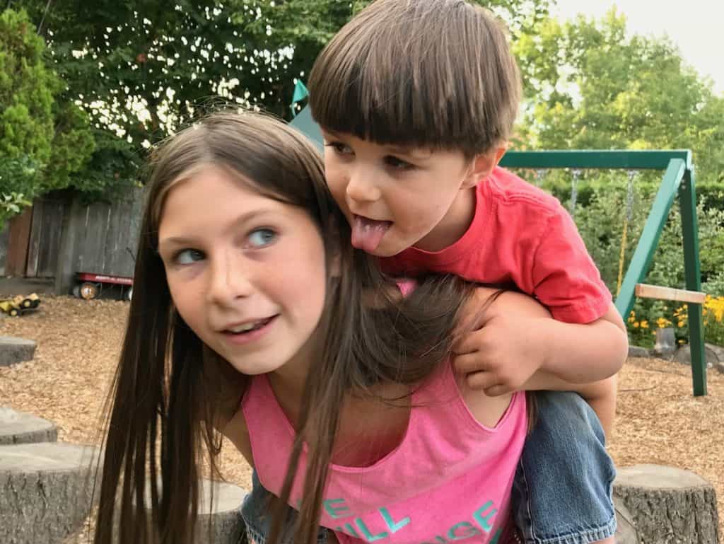 girl giving toddler a piggyback ride. good sibling relationships.