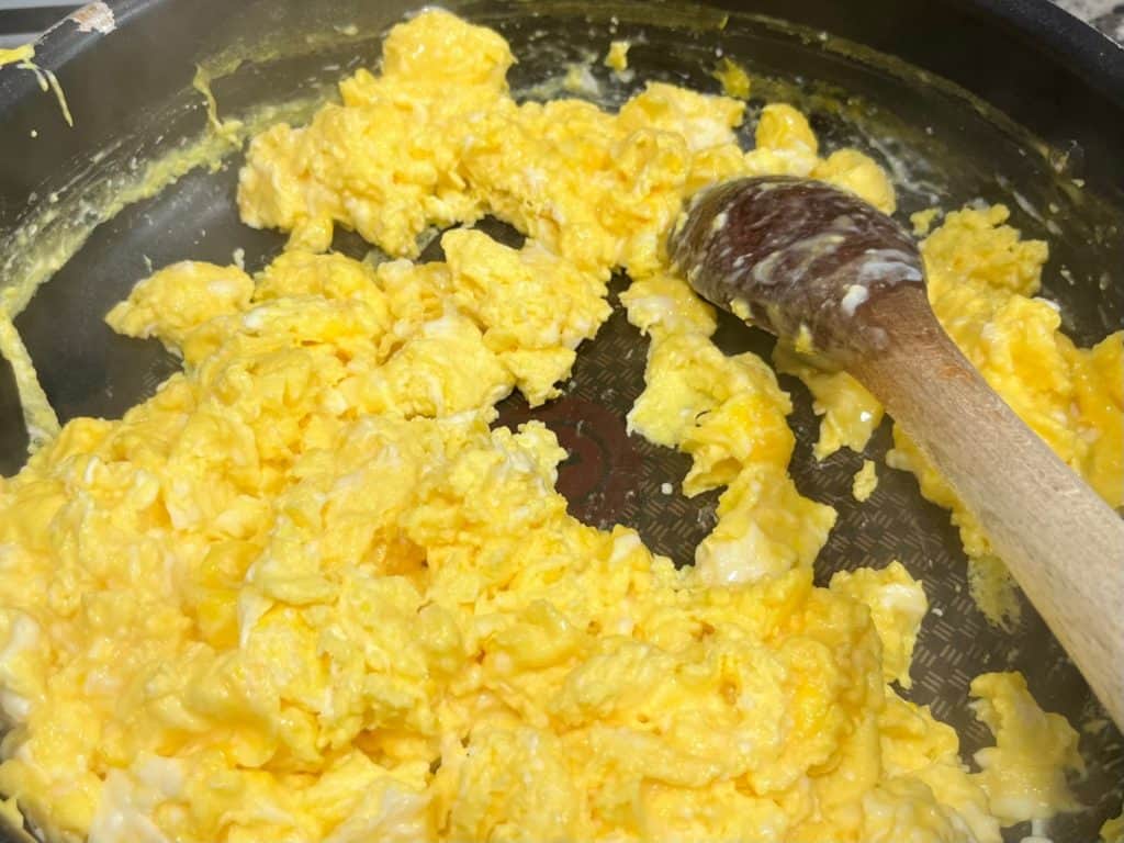 Scrambled eggs in a pan with a wooden spoon. Simple camping lunch ideas or camping breakfast ideas.