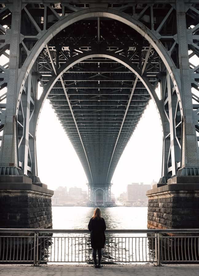 A woman looks out at the river under the enormous framework of the Williamburg Bridge. The Williamsburg Bridge is one of the highest bridges in the US. 