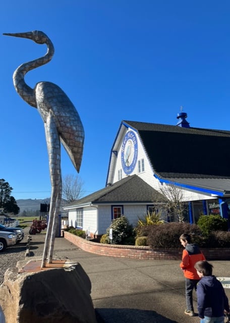 Blue Heron Cheese Company building with giant heron statue and boys in front