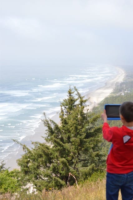 A boy uses his ipad to take a picture of the amazing view from the top of Cape Lookout. Cape Lookout is one of the best things to do on the Oregon Coast with kids.