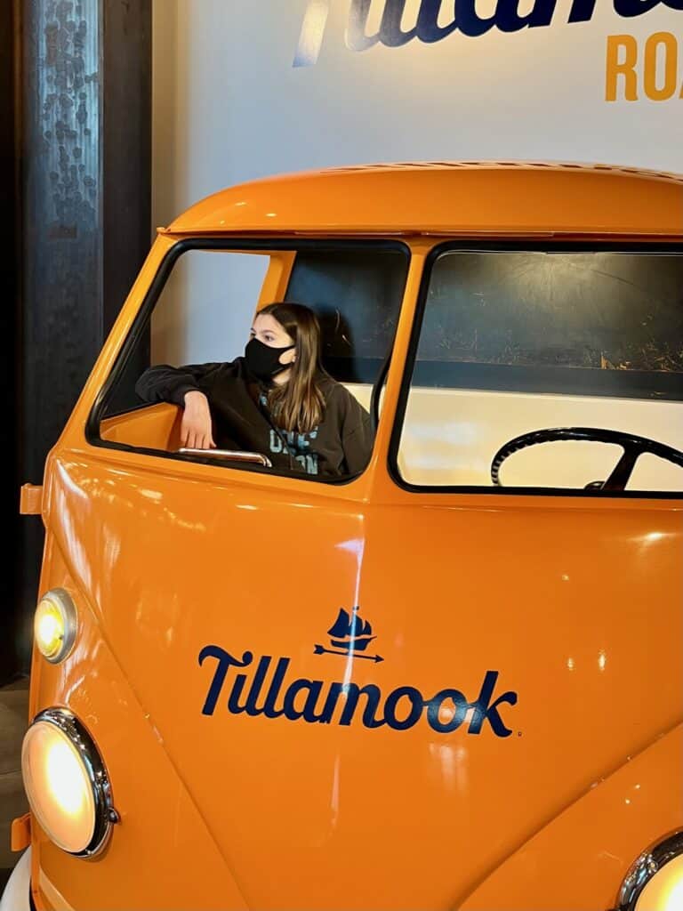 Girl wearing a mask sitting in the orange Tillamook van.