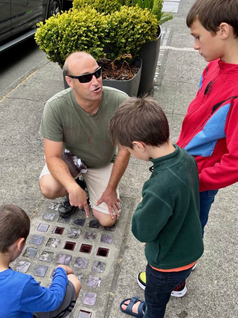 Brian explaining to the boys how the purple square glass skylights on a sidewalk in Astoria Oregon indicate the presence of an underground location.