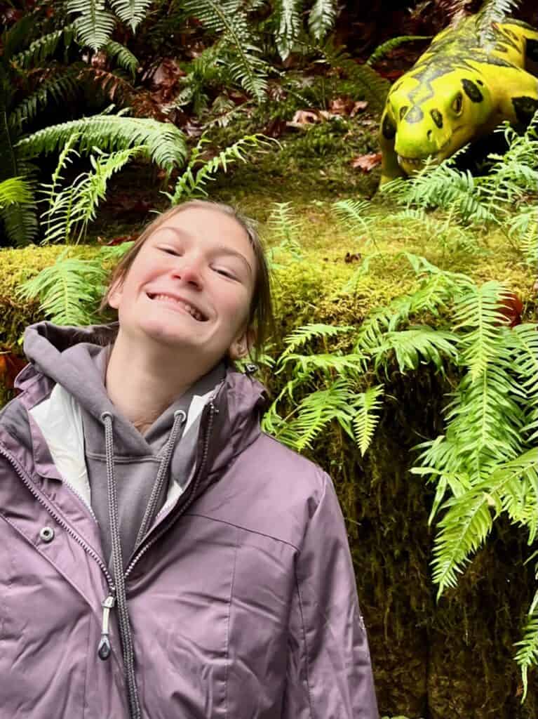 Our oldest daughter grins in front of a giant dinosaur at Prehistoric Gardens in Oregon.