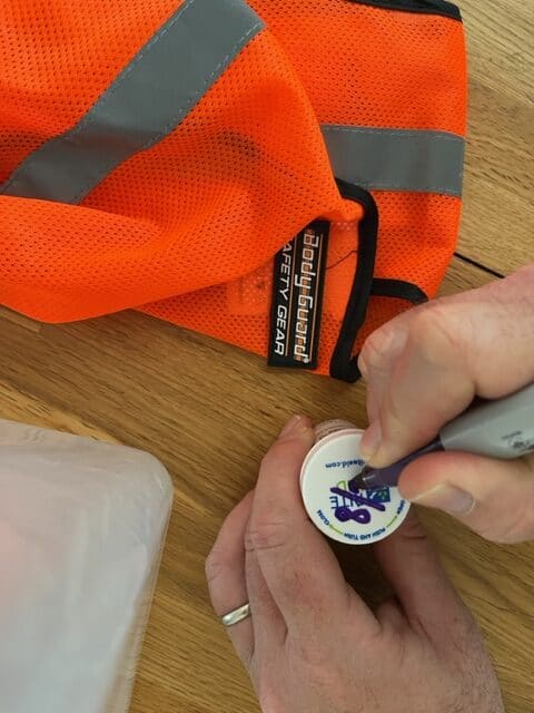 A reflective vest sits beside two hands as they date medications for a car emergency kit. People are wise when they carefully consider what to pack in a car emergency kit.