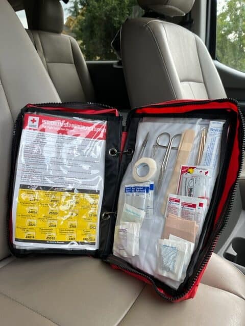 A first-aid kit sits upright on a passenger seat. A well-stocked first aid kit is a key part of every car emergency kit.