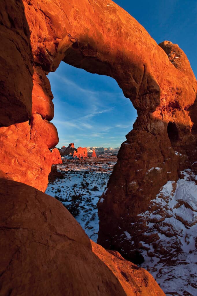 A natural arch frames a snowy scene at Arches National Park.