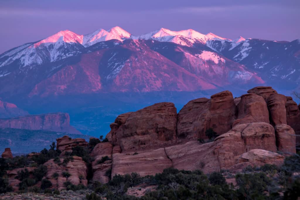 Snow-covered mountains form the background of Arches National Park. Arches National Park is one of the best national parks to visit in November and December.