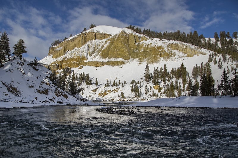 A river flows beside a snow-covered bluff at Yellowstone National Park. 