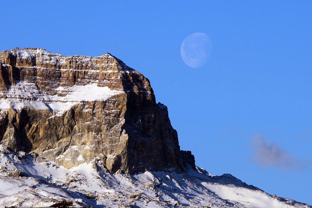 A winter moon hovers over Glacier National Park. Glacier National Park is one of the best national parks to visit in November and December.