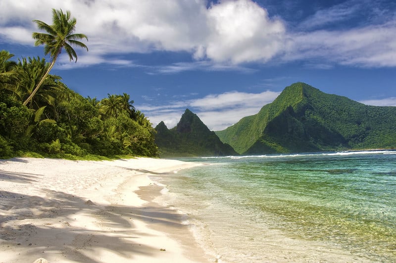 Palm trees line a white sand beach at the National Park of American Samoa. The National Park of American Samoa is one of the best national parks to visit in November and December.