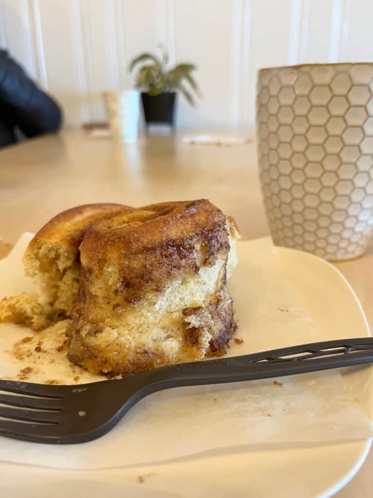 Partially eaten cinnamon roll with a mug of coffee behind. Little Leaf Cafe in Silverton Oregon.