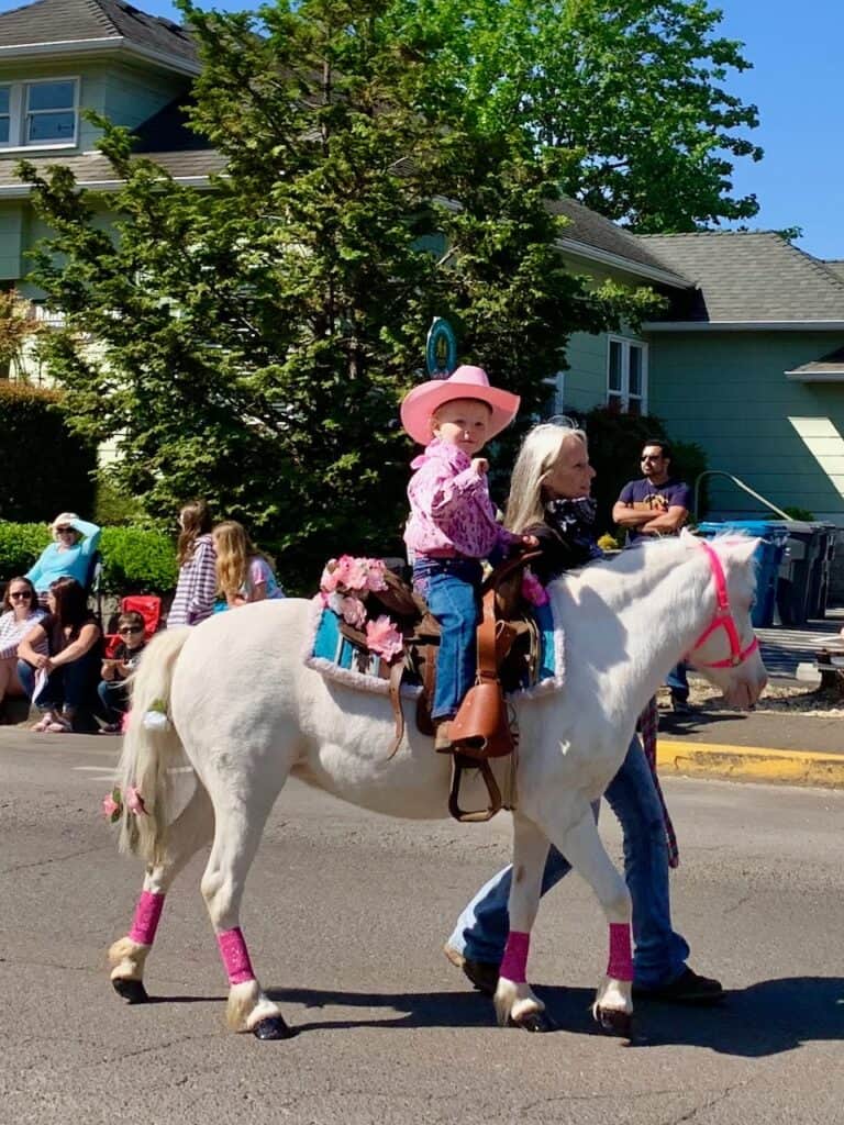 Little girl on a horse in pink cowgirl clothes walking in a parade. 