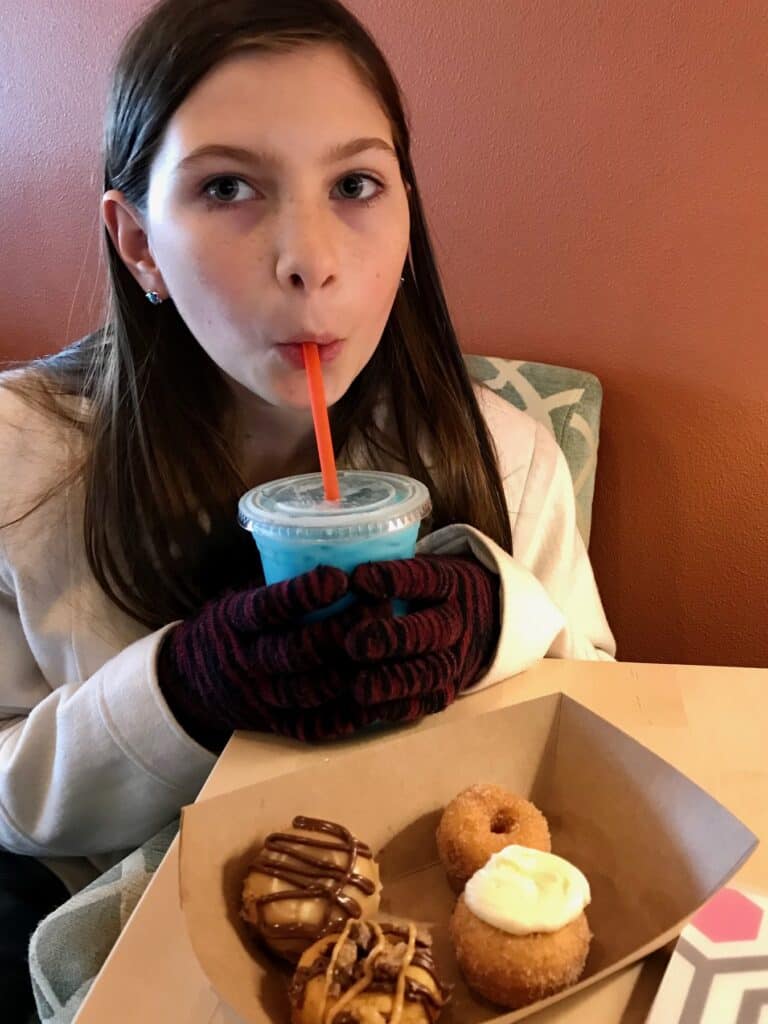 Our second daughter sips a blue drink with mini donuts in front of her at Gear Up Coffee.