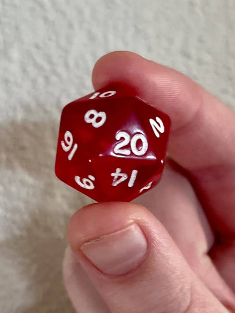 20-sided red D&D die held between the thumb and forefinger.