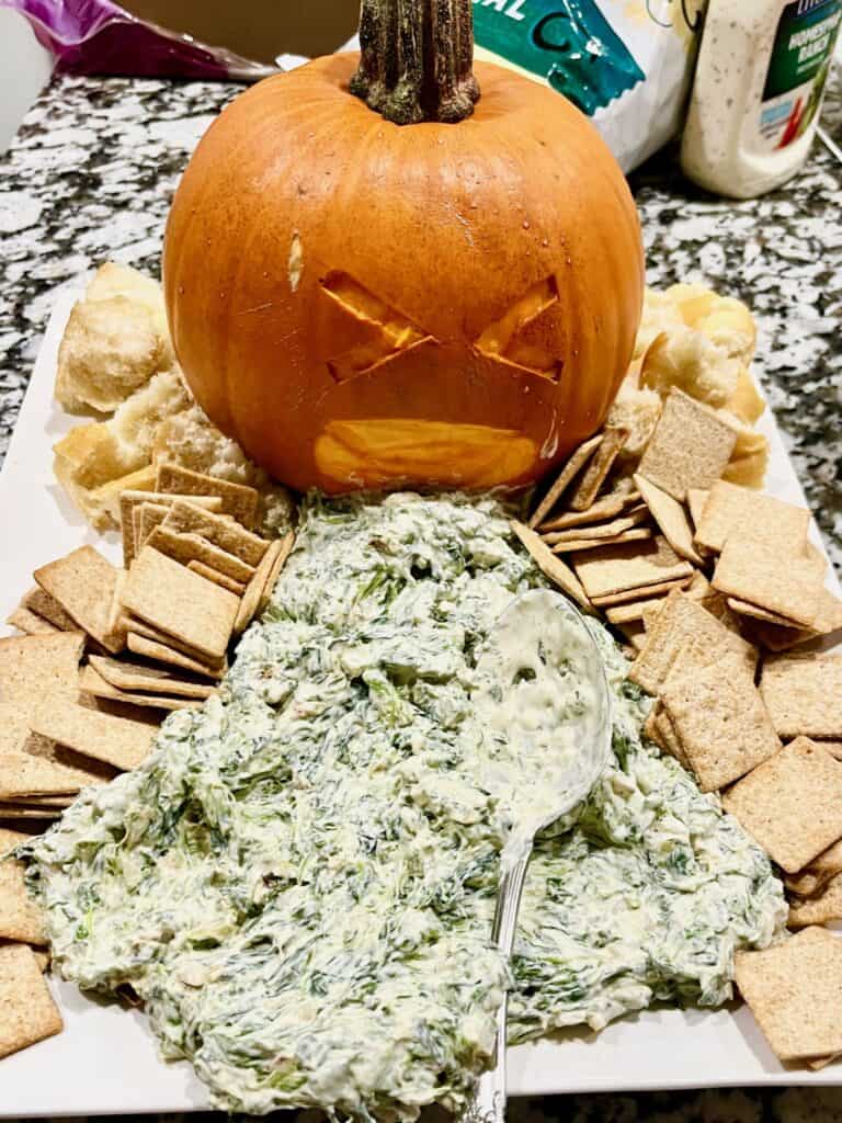 Spinach dip with crackers and bread with a carved pumpkin behind. Halloween activities for teens.