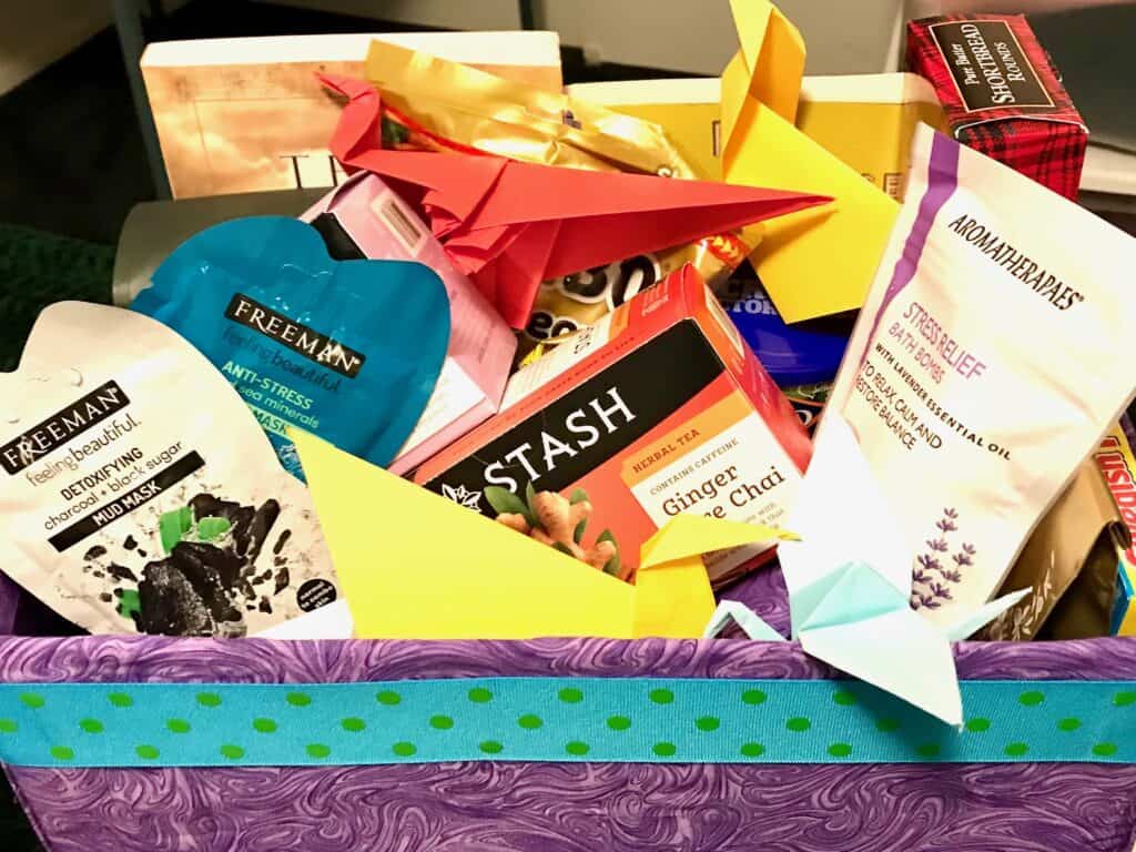 A gift basket with tea, mud masks, cookies, gummy bears and origami for self-care.