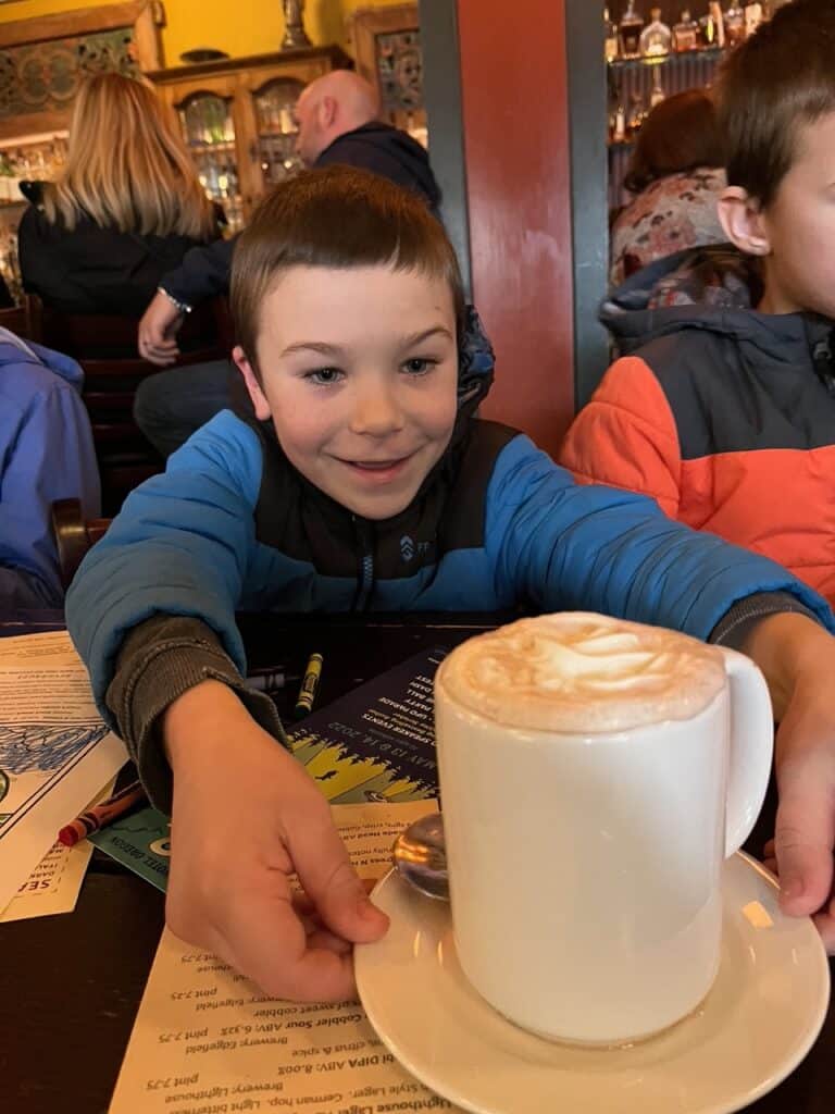 Our son smiles at a tall mug of hot coco at McMenamins Pub. McMenamins is one of the best breweries in McMinnville and Carlton.