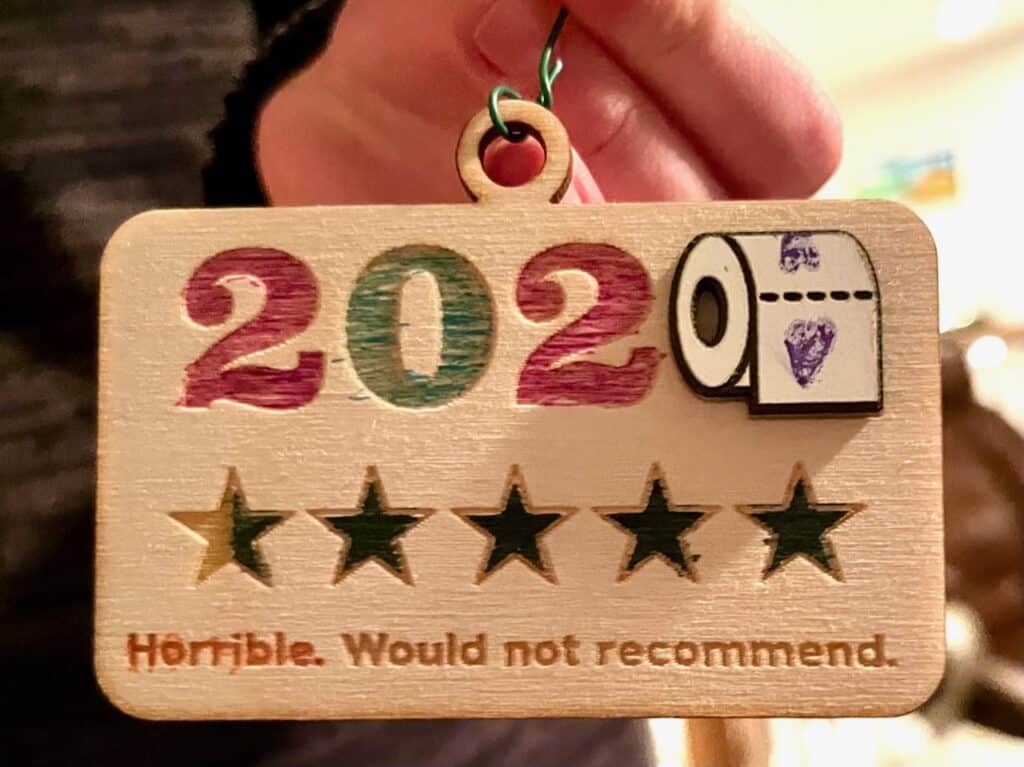 Wooden Christmas ornament shows 2020 with a roll of toilet paper and a half star rating. Underneath are the words "Horrible. Would not recommend"