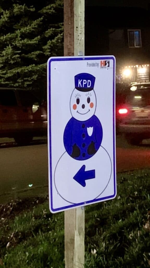Snowman sign on a stop sign with a hat that reads "KPD" and an arrow.