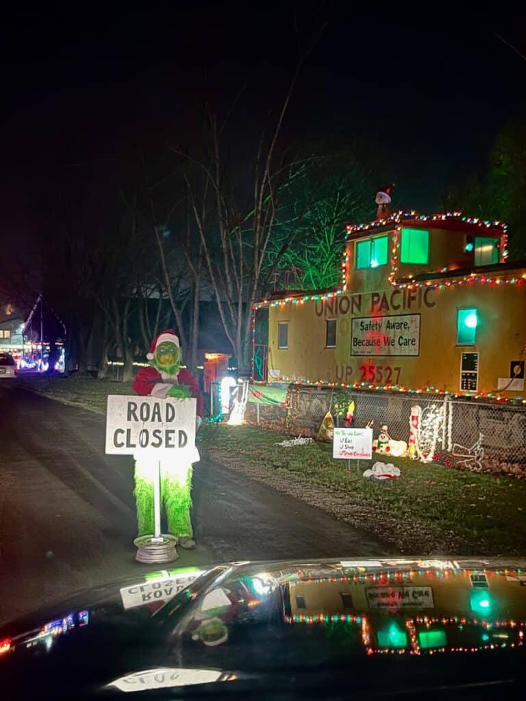 View from inside our van showing the Grinch standing in front of a road with a "Road Closed" sign next to a historic caboose. Best Christmas lights in Salem Oregon.
