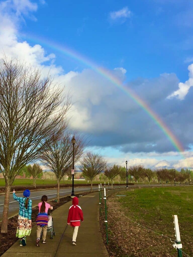 Three of our kids walking on a sidewalk towards a rainbow in the sky.