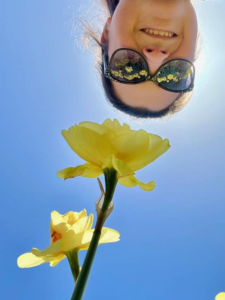 Jenn upside down with blue sky behind and daffodils below.