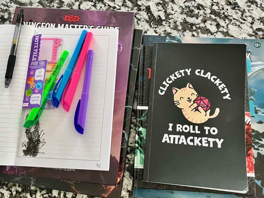 Dungeon Master planning tools, including two journals, colored pens, sticky notes, and D&D rulebooks on a countertop.