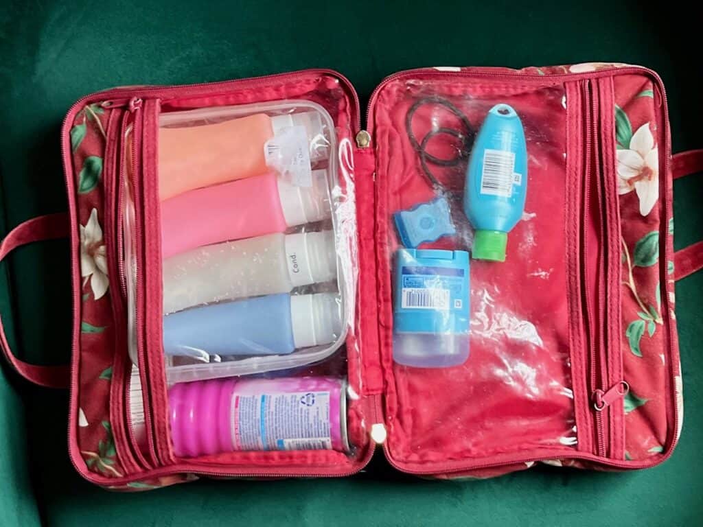 Red toiletries bag with a variety of shampoos, lotions and other skincare items.