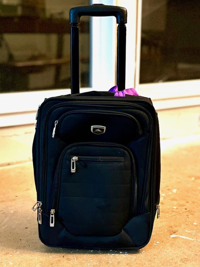 Black carry-on sized suitcase with a purple ribbon.