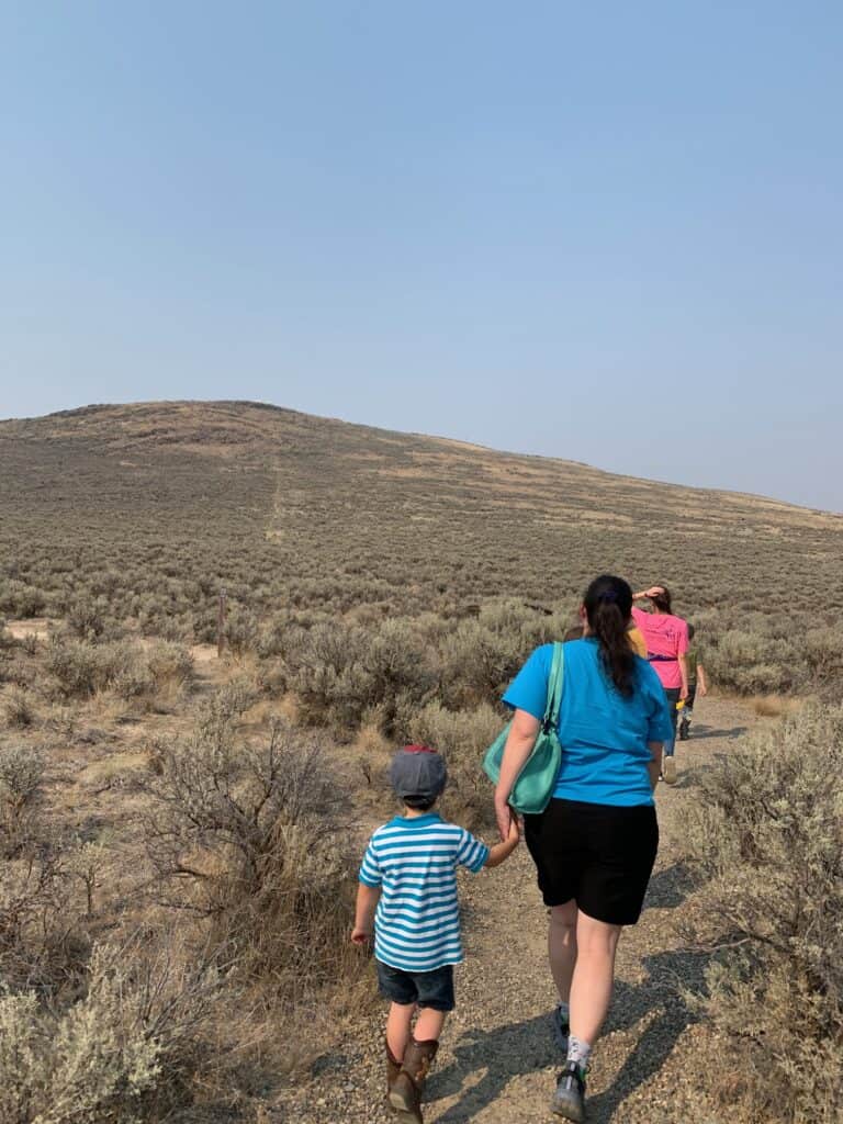 Jenn and the kids walking through desert scrubland towards Oregon Trail ruts on a distant hill.