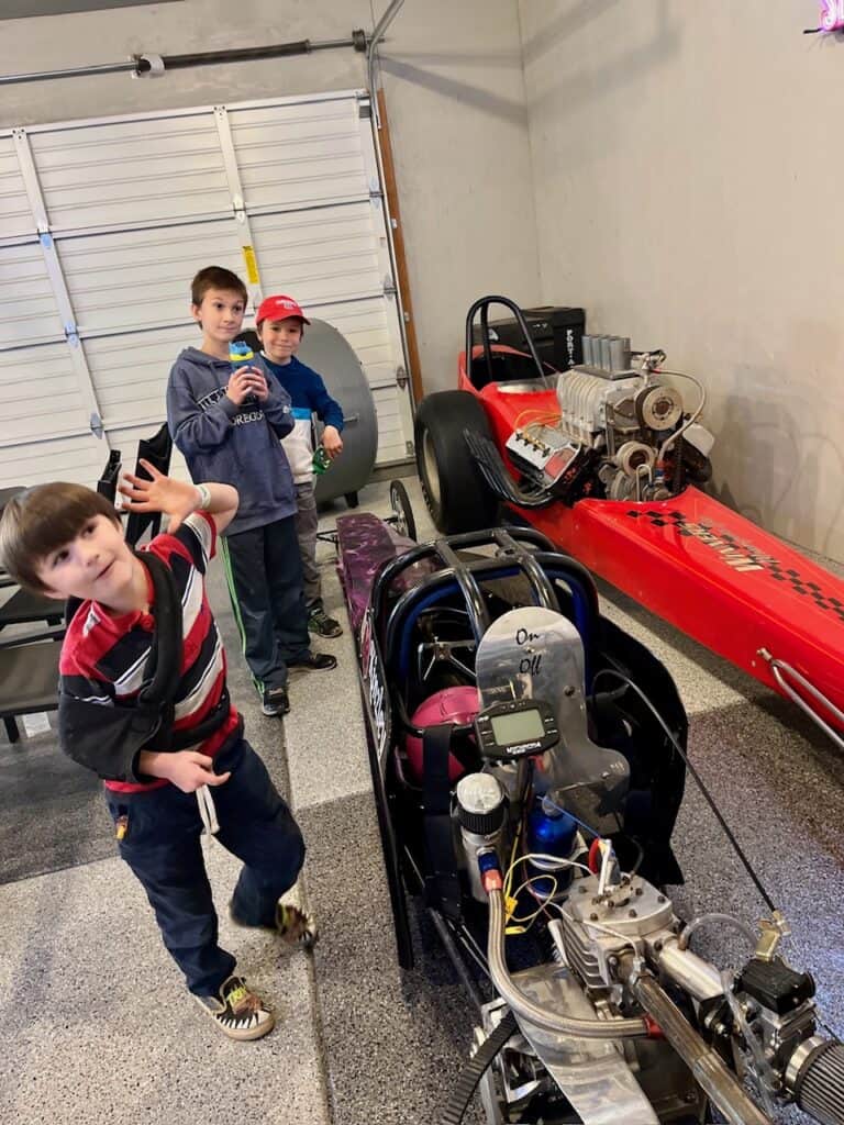 Our boys next to a dragster in a garage at the Woodburn Dragstrip.