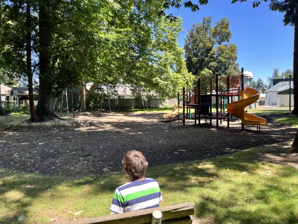 Our son sitting on a bench looking towards Settlemier Park playground