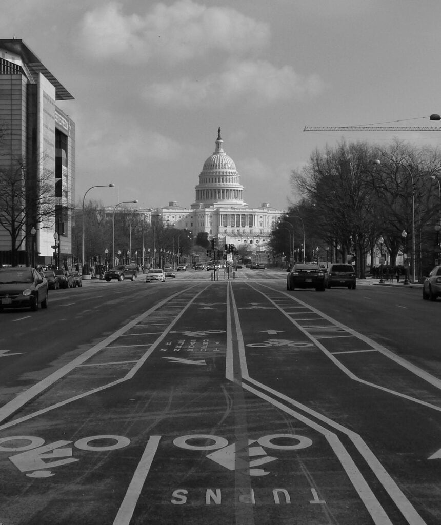 A black and white photo shows the US capitol. and the end of Pennsylvania Avenue.