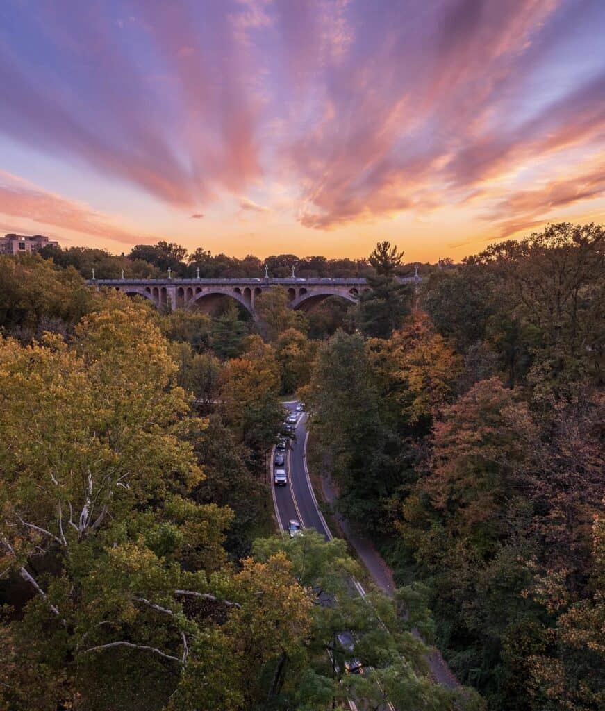 A dusking sky crowns a bridge and a forested parkland at Rock Creek Park.