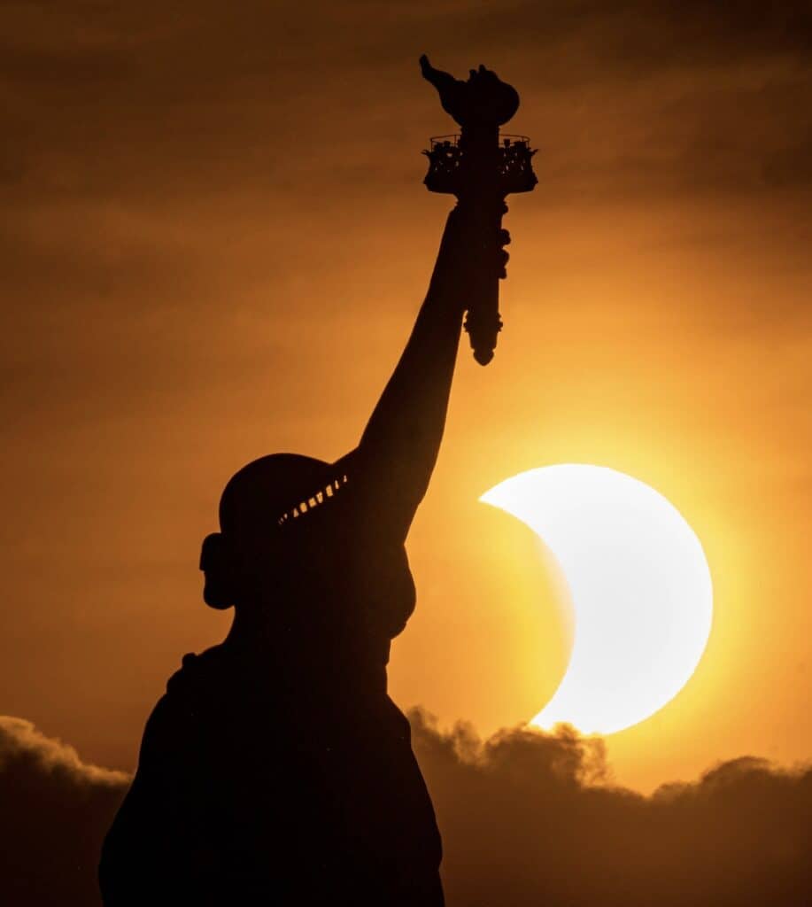 A Silhouette of the Statue of Liberty stands in contrast to a solar eclipse.