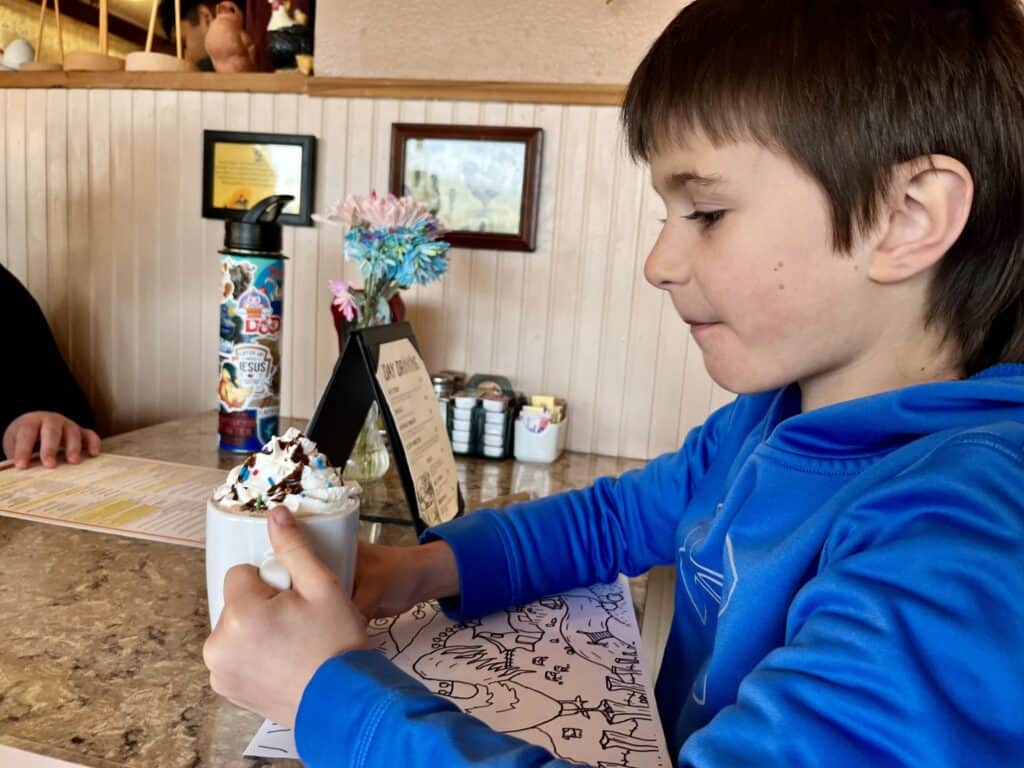 Our son holds his hot cocoa mug topped with whipped cream, sprinkles and chocolate syrup