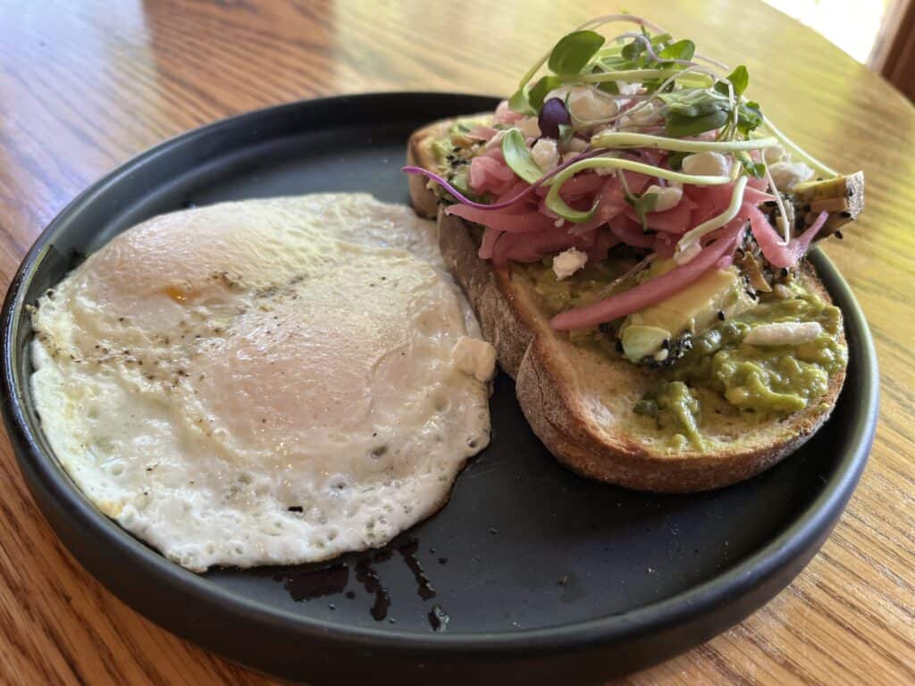 Avocado toast and two eggs on a black plate