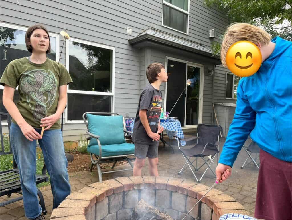Teens roasting marshmallows at a backyard fire pit