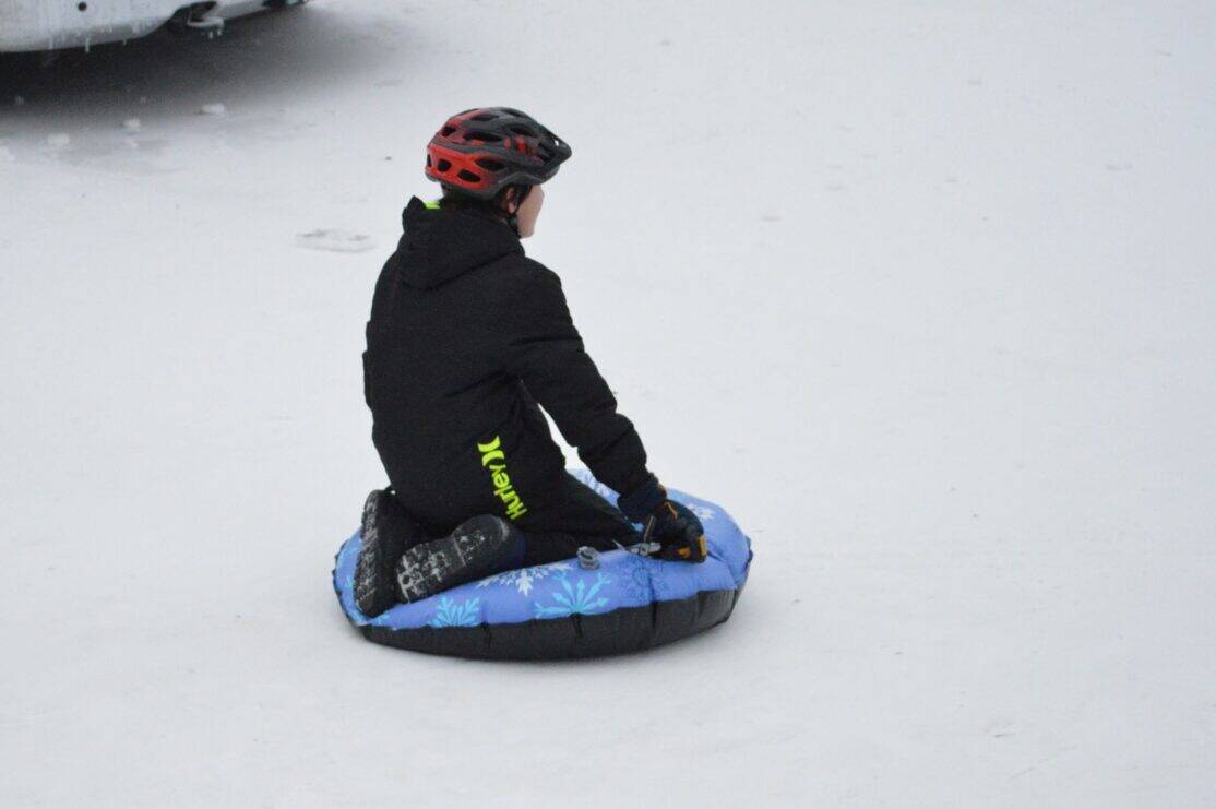 Teen boy on a snow tube wearing a helmet.