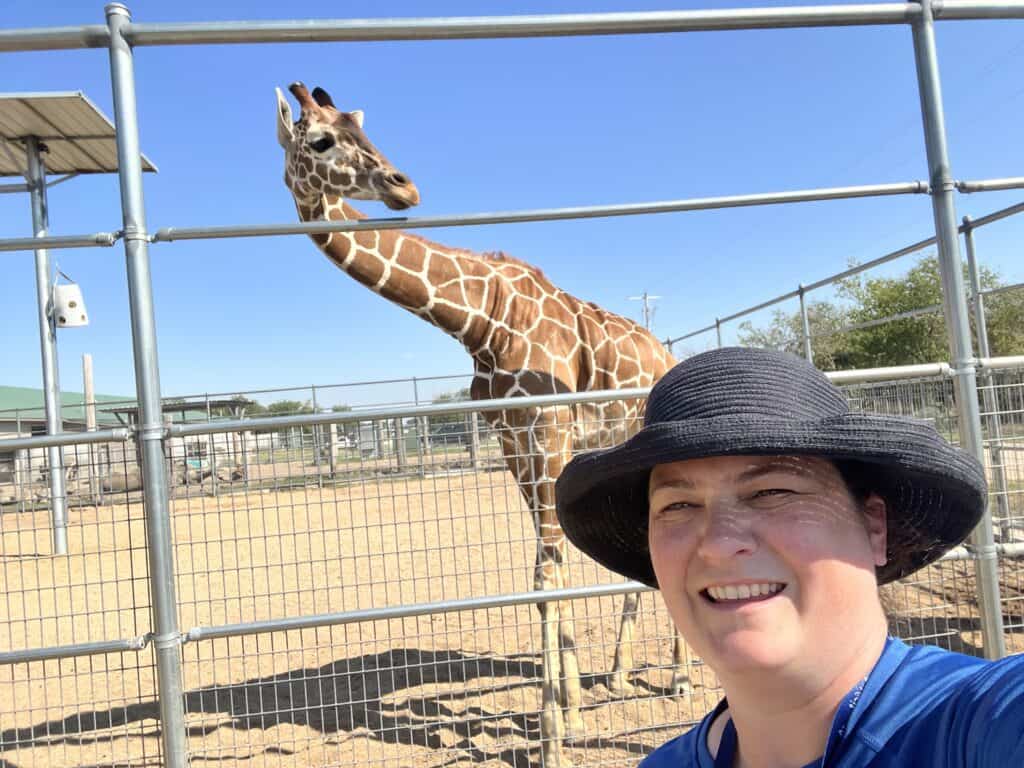 Jenn with giraffe behind inside enclosure