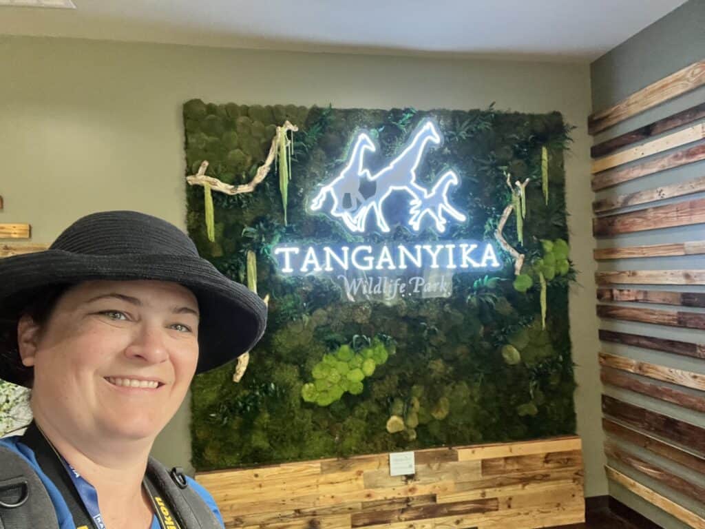 Jenn in black hat with lighted Tanganyika Wildlife Park sign in the background
