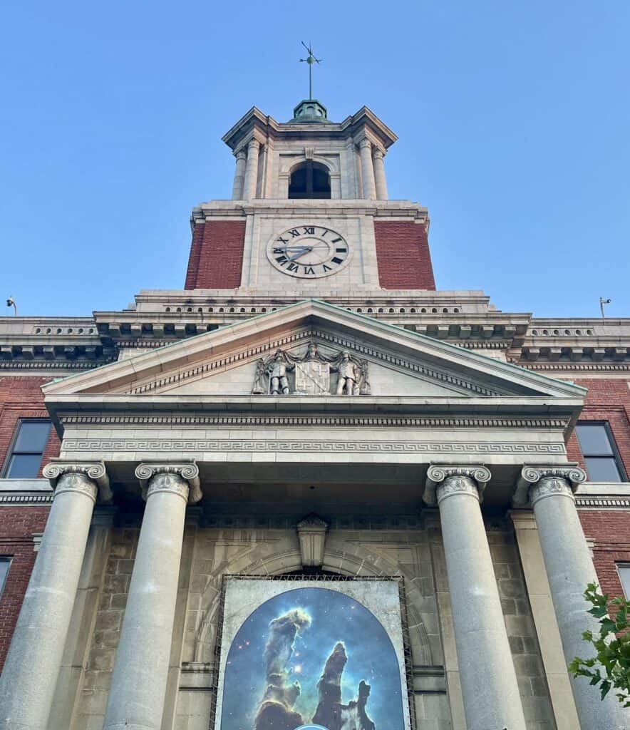 An imposing clock tower towers over a historic bank building at Baltimore National Heritage Area, Manyland.