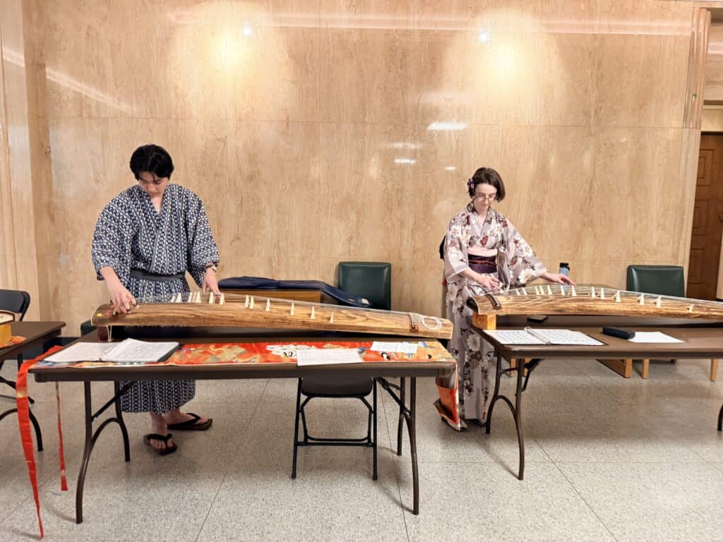 Two people in traditional Japanese kimonos demonstrate playing the koto, a traditional Japanese stringed instrument, inside the Oregon Capitol