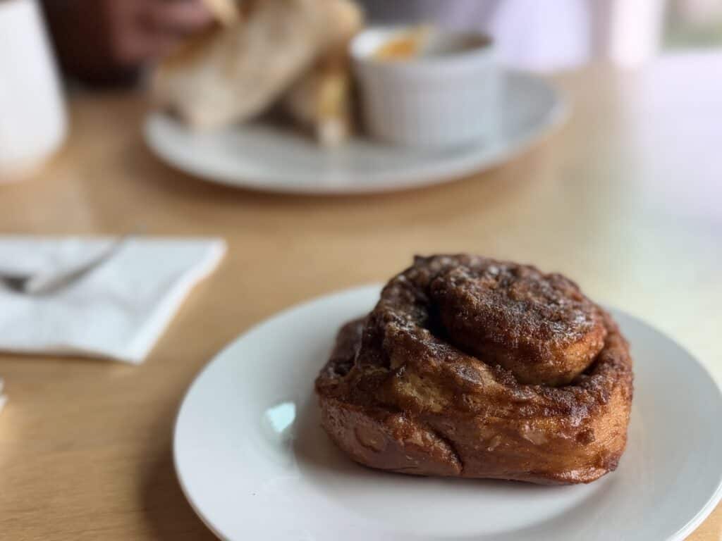 Breakfast table with cinnamon roll in foreground, breakfast burrito in background