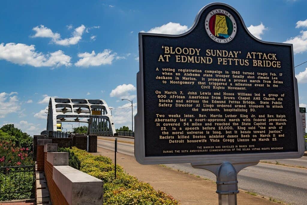 A historic marker stands at the foreground in a picture of the Edmund Pettus Bridge, a key site along the Selma to Montgomery National Historic Trail.