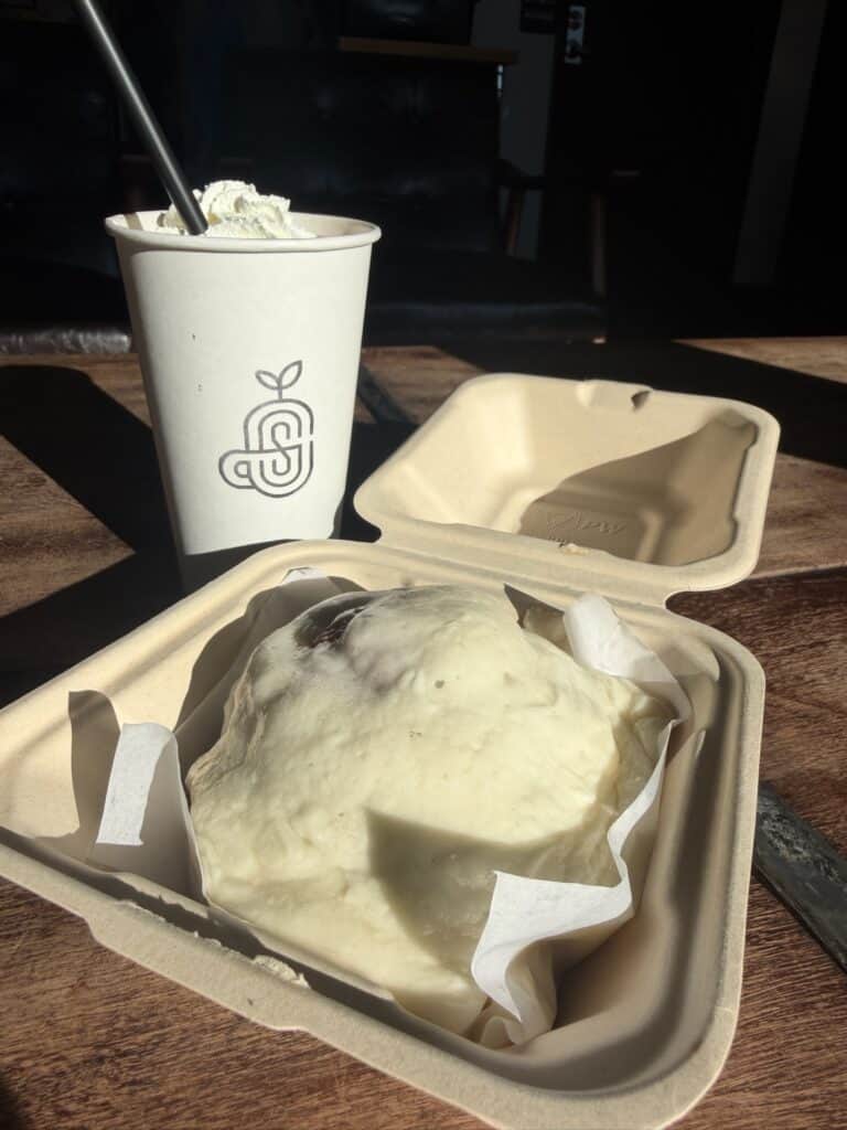Solvivo paper coffee cup and a cinnamon roll covered with cream cheese frosting.