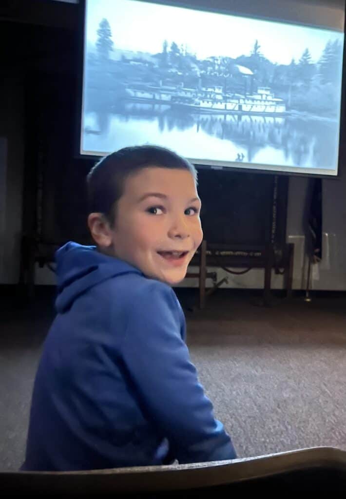 My son looks back at us with an excited look while watching a historic documentary at Champoeg State Park in French Prairie.