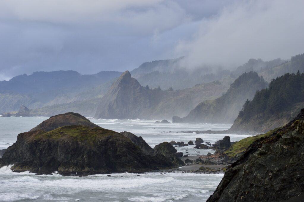 Surging waves pound against rugged, forested bluffs near Sisters Rock State Park.